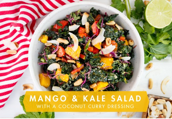 Kale salad with mango chunks, shredded red cabbage, with a creamy dressing in a white serving bowl.