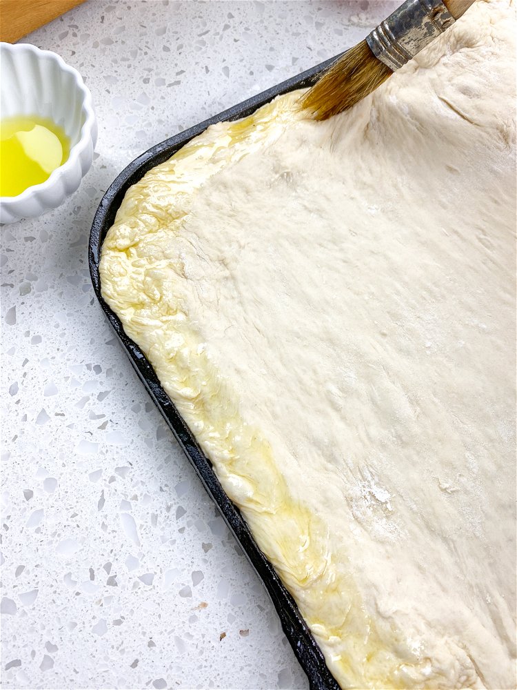 Image of Brush remaining olive oil around the perimeter of the dough,...