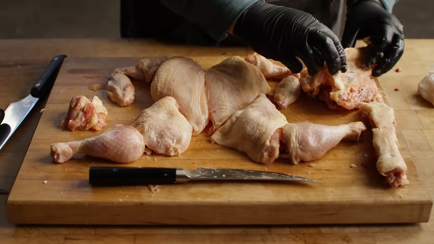 Using kitchen knife to cut raw chicken leg away from flesh