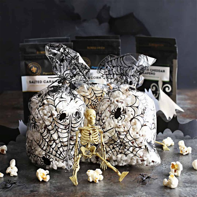 Image of Fill spiderweb themed plastic bags with popcorn and attach seasoning...