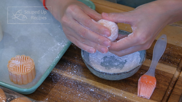Image of Brush the mooncake pattern with flour to prevent sticking. Coat a mooncake ball with a little bit of cake flour and shake off the excess. Shape the ball into a cylinder, then put it into the mooncake presser. Press it...