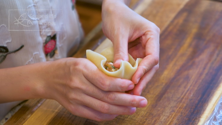 Image of Put a filling in the middle of the wrapper. Lightly wet the edge. Use your fore finger and thumb to keep squeezing and pushing the wrapper up. Pinch the edge and close the mooncake. Do the same thing to wrap...