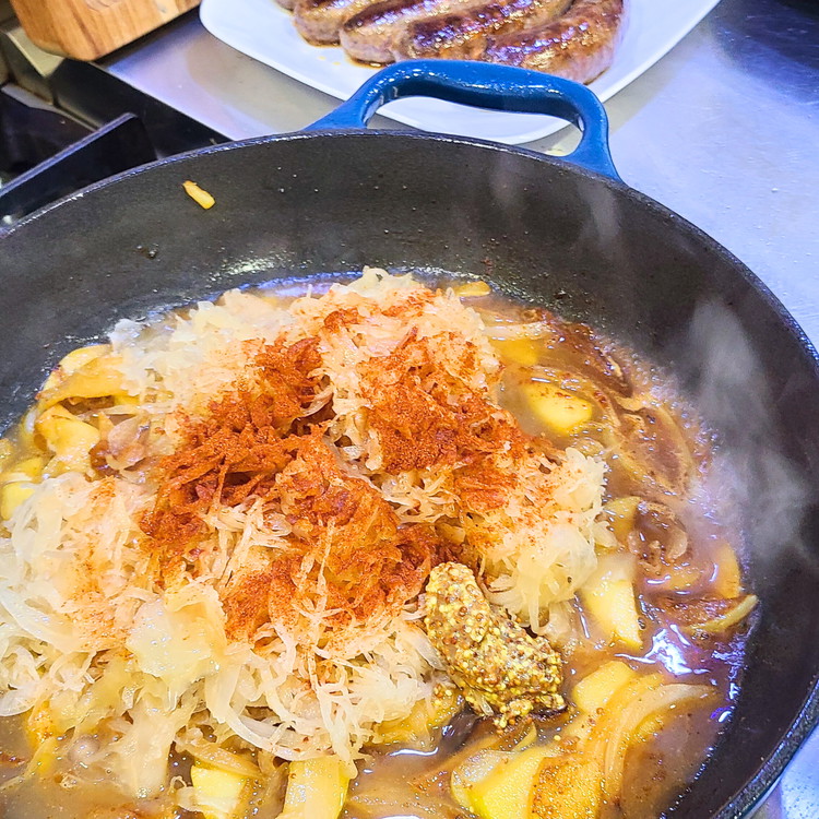 Image of Add the drained sauerkraut to the skillet with the onion, apples and garlic. Add the Dijon mustard, paprika, salt and pepper. Pour in the chicken or vegetable broth and white wine (if using). Stir to combine all the ingredients.