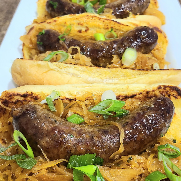 Image of To serve, spread a nice layer of the seedy dijon on the toasted bun, add a generous serving of the sauerkraut mixture and top with a sausage and a sprinkle of green onion for a little extra crunch and colour.