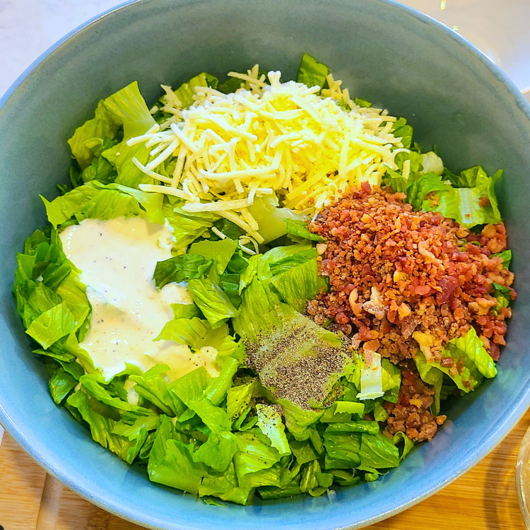 Image of In a large bowl, combine the chopped romaine lettuce, parmesan, bacon bits and Caesar dressing. Toss until the lettuce is well coated.