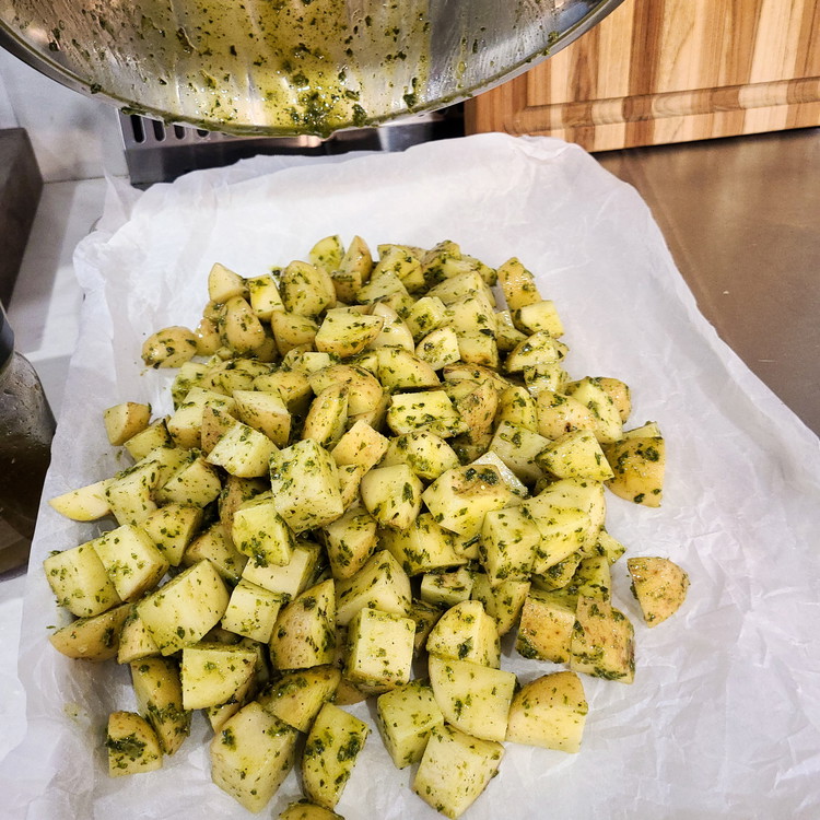 Image of In a large bowl, toss the potatoes with the pesto, olive oil, salt, and black pepper until they are well coated. Spread the potatoes in a single layer on a parchment-lined baking sheet.