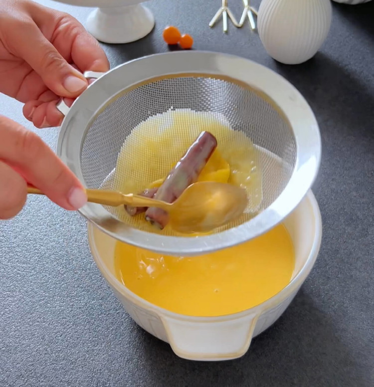 Image of Den Topf vom Herd nehmen und den vorbereiteten Zuckersirup nach und nach in die Milchmischung einrühren, während Sie ständig rühren. Lassen Sie die Mischung etwa 10 Minuten ziehen, dann entfernen Sie die Zimtstangen und Zitronenschalen.