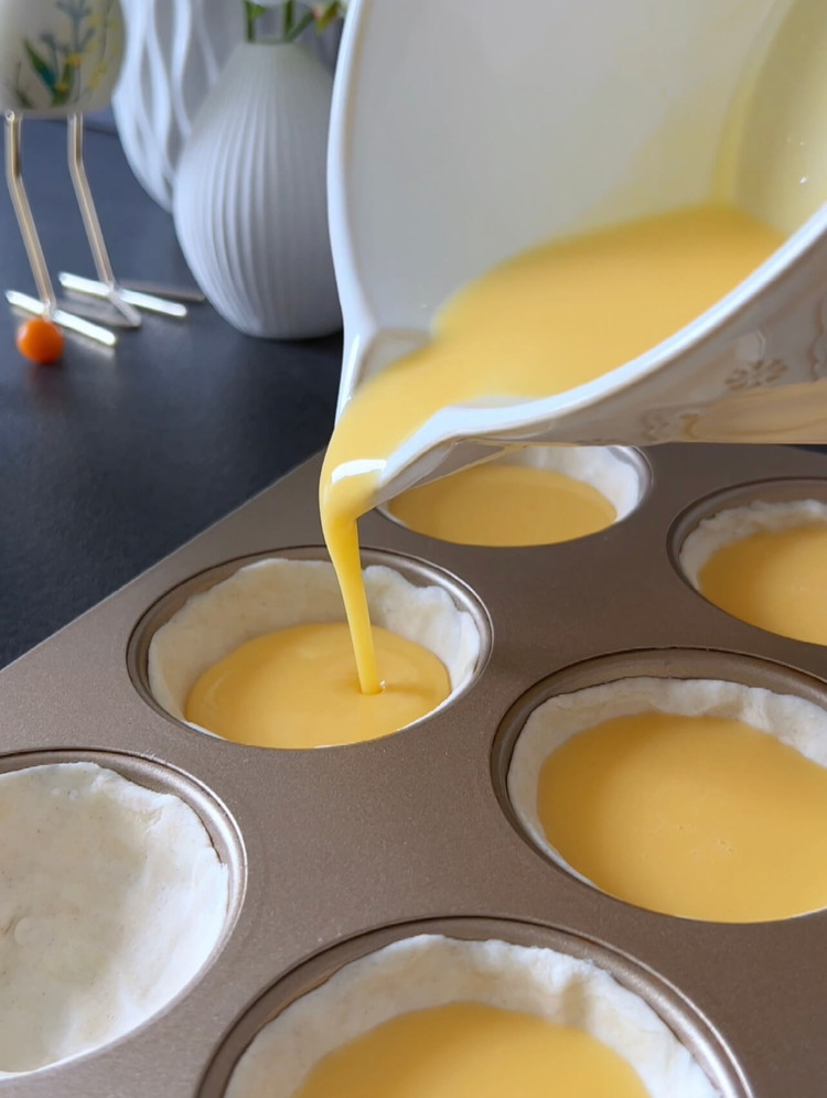 Image of Nehmen Sie die vorbereitete Muffinform und gießen Sie den Pudding gleichmäßig in die Blätterteigvertiefungen, wobei Sie etwas Platz um die Ränder lassen.
