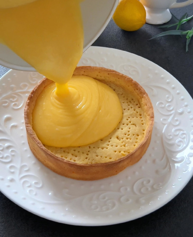 Image of Zitronensaft, Schale, Zucker und Eier in einem Topf vermengen. Bei mittlerer Hitze unter ständigem Rühren zum Kochen bringen, bis die Mischung eindickt. Vom Herd nehmen, die Butter einrühren und abkühlen lassen. Die abgekühlte Zitronenfüllung auf den Tarteboden verteilen und 2...