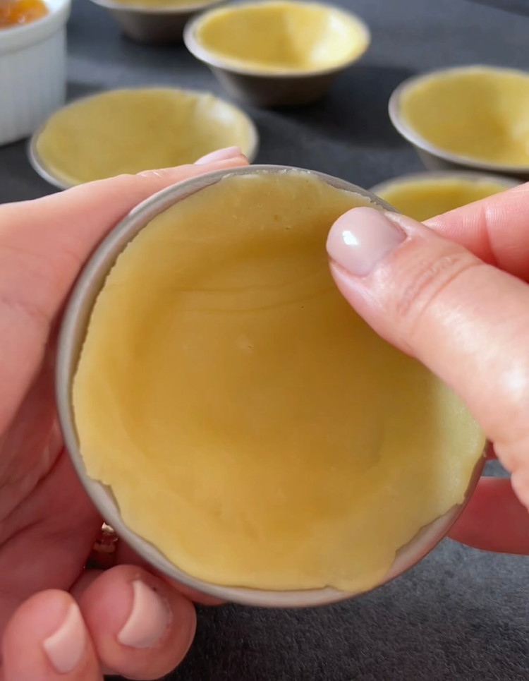 Image of Coloca cada círculo de masa en un molde para tartaletas engrasado, creando pequeñas conchas de masa.