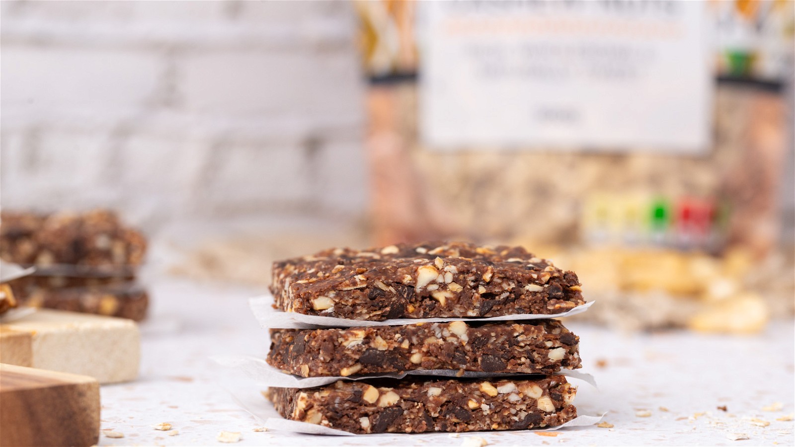 Three homemade Chocolate Cashew Energy Bars stacked atop one another, with a bag of Essina Wholefoods raw cashew nuts visible in the background, showcasing the key ingredient in these nutritious and delicious homemade energy bars