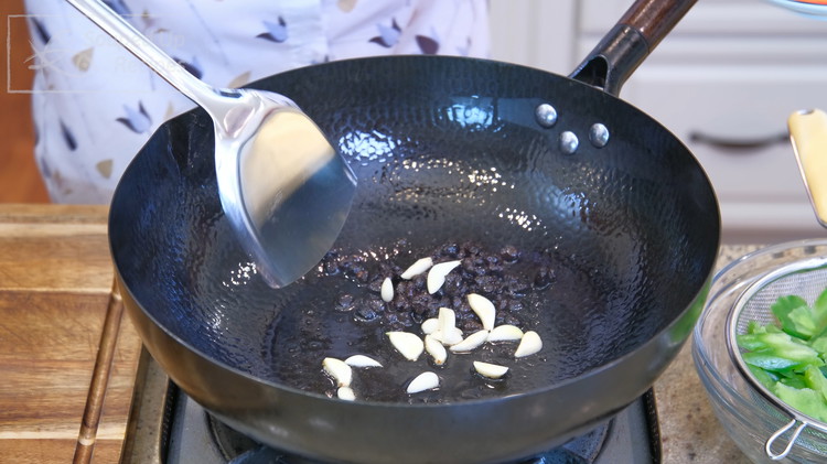 Image of Add the reserved fermented black bean and oil mixture from the can and garlic slices to a wok. Stir until fragrant.