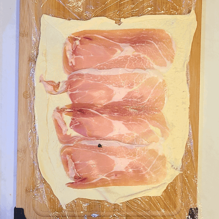 Image of Place plastic wrap down on a work surface, overlapping so that it’s twice the length and width of the tenderloin. Lay out 1 sheet of puff pastry, make sure it’s big enough to cover the whole tenderloin. Arrange the prosciutto...