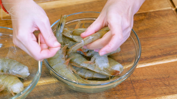 Image of Devein the shrimp by sticking a toothpick underneath and pulling it out. I will not peel the shell because it helps keep the shrimp moist during the cooking process.