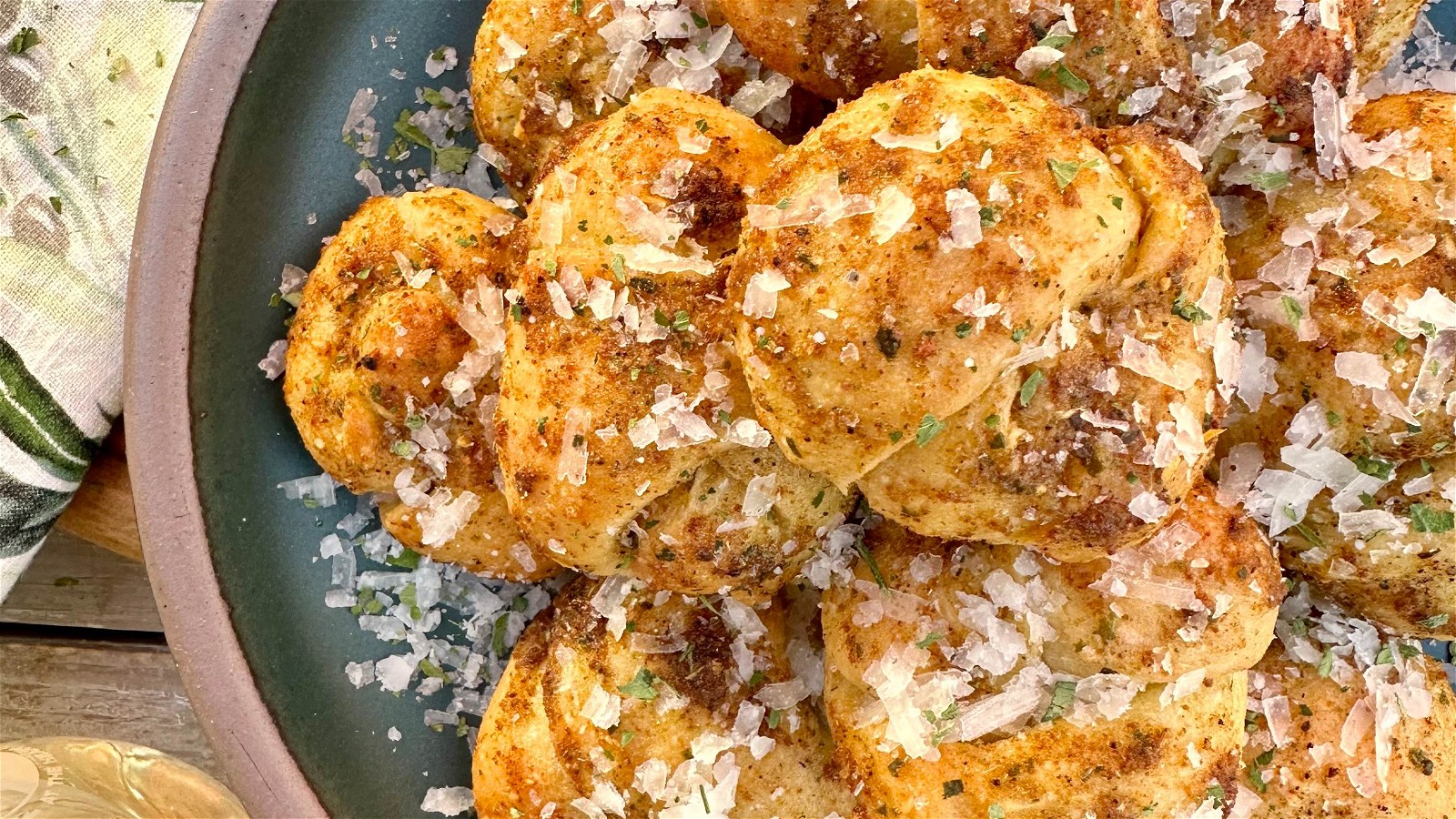 A ceramic plate of garlic knots covered in butter, Magic Garlic Dust, and herbs.