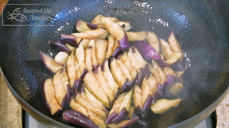 Image of Slide the eggplant into the wok. Since you flipped the eggplant ahead, the skin side should now be in contact with the wok bottom. That is the trick to retain the purple color.