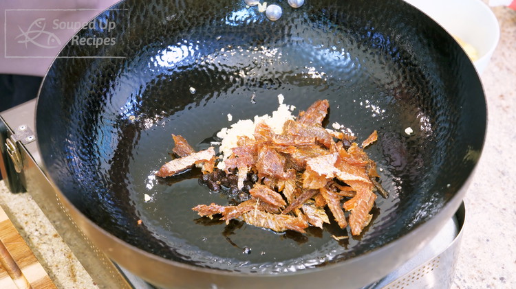 Image of To the same wok, add the oil from the fried dace can, along with 1.5 Tbsps fermented black beans, 2 Tbsps minced garlic, and the fried dace. Stir for 20 seconds or until fragrant.