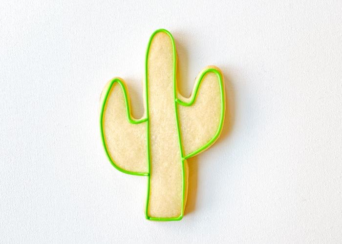 Image of Outline the two arms of the cactus with green piping consistency icing. By outlining the three areas separately, you will achieve more definition between the cactus arms and trunk.