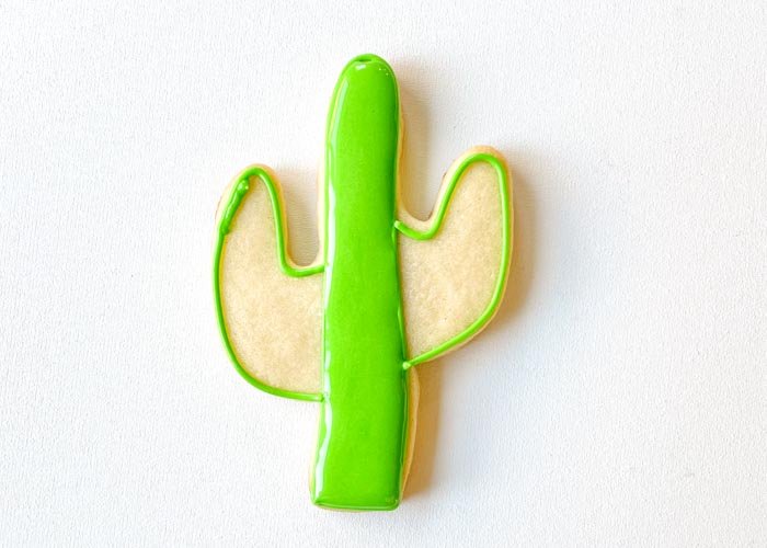 Image of Fill the center of the cactus with green piping consistency icing. Use a scribe tool or toothpick to move the icing around, ensuring full coverage and getting rid of any air bubbles.     Wait for the flood to dry 30-60 minutes, or until it is starting to crust over.
