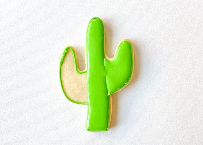 Image of Fill the one arm of the cactus with green flood consistency icing. Use a scribe tool or toothpick to move the icing around, ensuring full coverage and getting rid of any air bubbles.