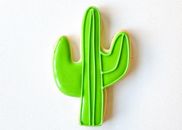 Image of Outline the shape and pipe one line on one arm of the cactus using piping consistency green icing, following the contours of the shape. Again, your base flood must be dry before doing this step to achieve definition.