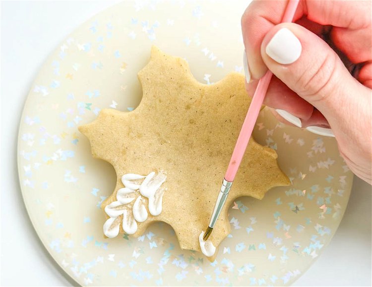 Image of Using the paintbrush, brush the middle of the dot of icing, dragging it towards the center of the cookie. We're aiming for a brushed look that still maintains the thickness of the original dot at the edge. We'll be continuing this motion to create a layered pattern design on the cookie.
