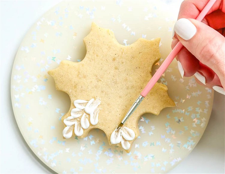 Image of Using the paintbrush, brush the two dots of icing diagonally towards the middle of the snowflake section, as shown in the photo. Continue piping and brushing until all six sections are filled, and you have a circle of empty space in the middle of the snowflake shape. Pro Tip: This design is great for beginners because it's very forgiving. You can easily adapt this design by making smaller or larger dots than I did (and using a smaller or larger brush). This design is about the artistic quality and will look great even if it isn't super precise. No two snowflakes are exactly the same, right?!