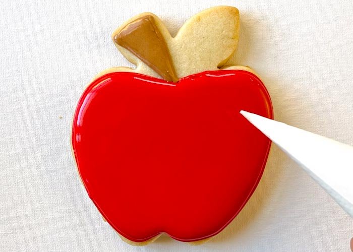 Image of Fill in the main part of the apple with red flood consistency icing. Use a scribe tool or toothpick to move the icing around to ensure full coverage.