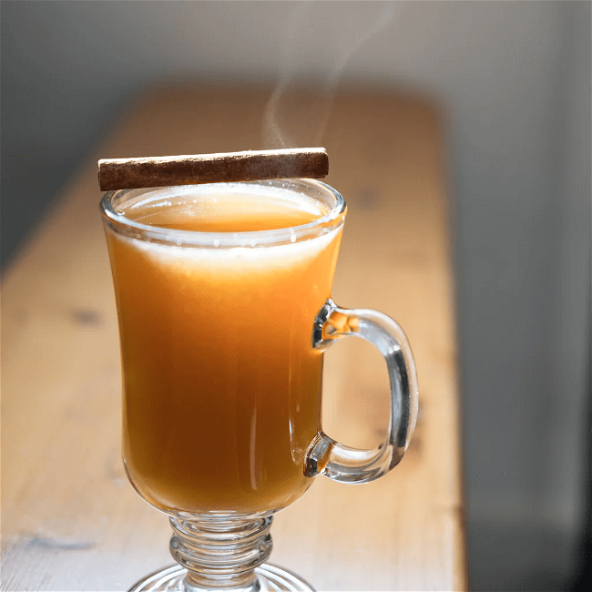 Deep orange hot toddy in a glass mug with a cinnamon stick on top