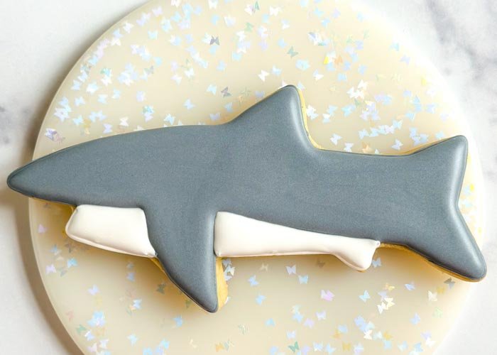 Image of Fill in the bottom portion of the shark with white flood consistency royal icing. Pipe some squiggles inside the shape to ensure the icing doesn't collapse as it cools.Let both sections dry a minimum of 1 hour before moving onto the next step.