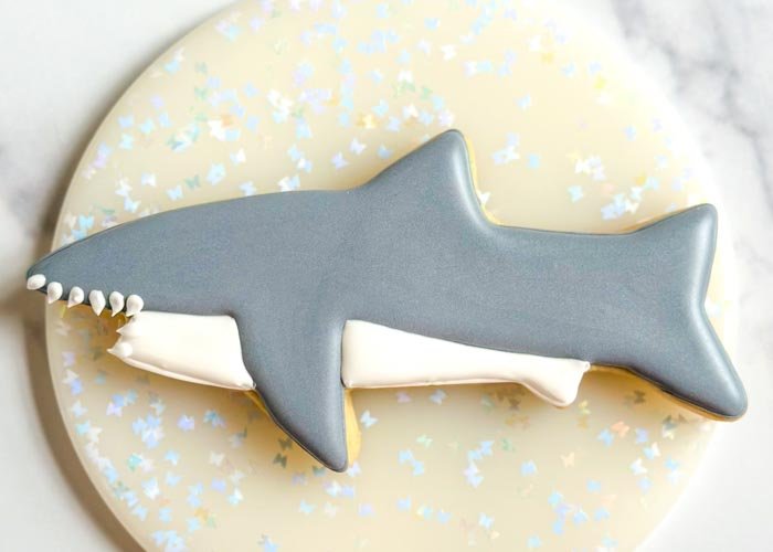 Image of Using white piping consistency royal icing, pipe dots on the shark's mouth and then use a scribe tool, or toothpick, to gently drag the icing to create sharp teeth.