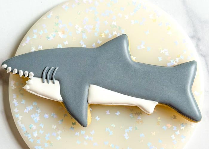 Image of Using gray outline consistency royal icing, pipe 3 identical curved lines between the shark's mouth and fin, as shown. These will be the gills of the shark.