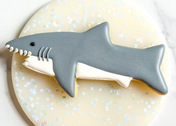 Image of Using black outline consistency royal icing, pipe a small dot above the last tooth for the shark's eye. Alternatively, you can use a small candy or nonpareils to create the eye.  