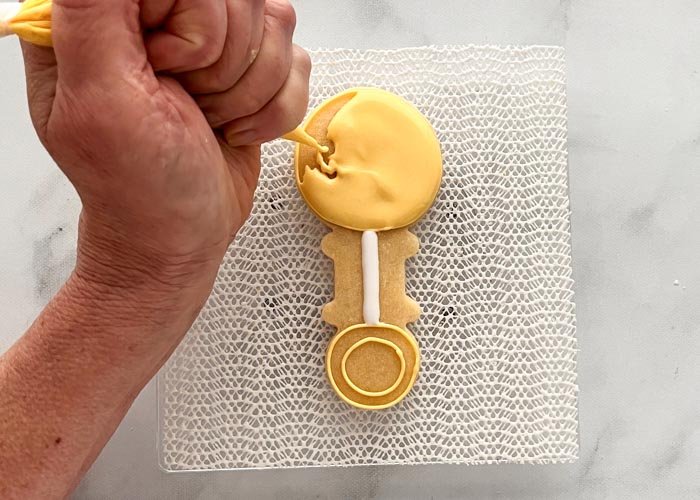 Image of Use yellow flood consistency icing to flood the top of the rattle, then the handle. 