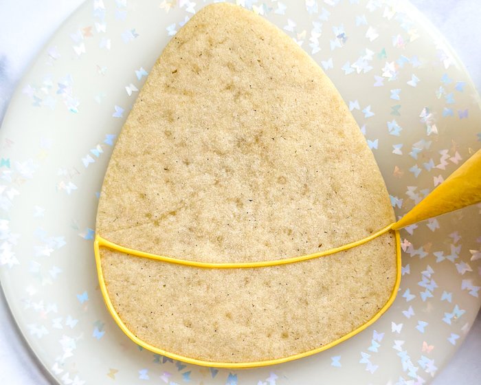 Image of Using yellow piping consistency icing, outline the bottom third of the cookie, as shown.