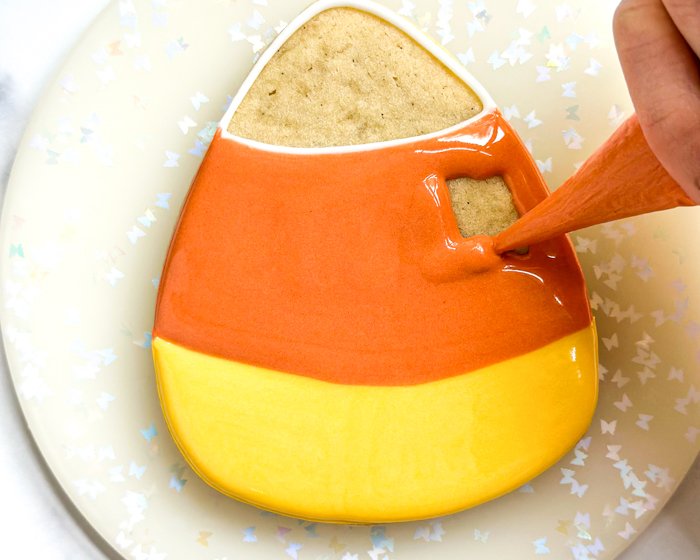 Image of While the yellow section is still wet, flood the middle section of the cookie with orange flood consistency icing.