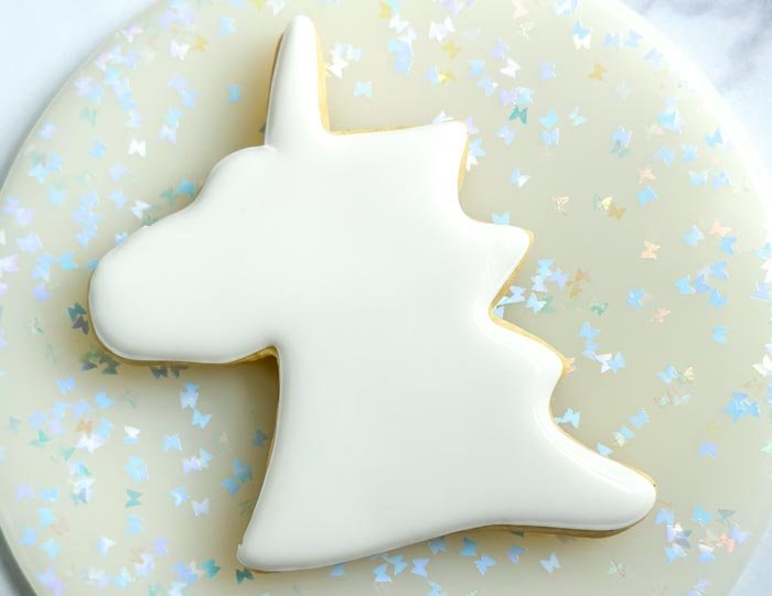 Image of Outline the entire cookie in white piping consistency royal icing. Pipe a squiggle of white piping consistency icing in the body of the unicorn, this will prevent the flood consistency icing from collapsing or cratering. Move immediately to the next step.