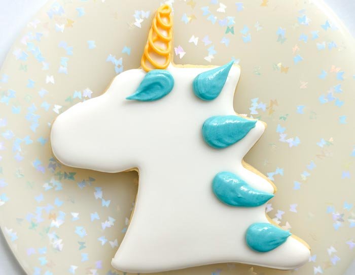 Image of Using yellow piping consistency royal icing, pipe the unicorn horn. Snip a tipless bag so that it has a fine point. Using this fine point, pipe a tight spiral to create texture in the unicorn horn.