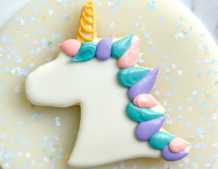 Image of Using the purple piping consistency royal icing, pipe the unicorn mane using the same technique as step 5 next to the blue icing you just piped. Let the icing dry for 30-60 minutes.