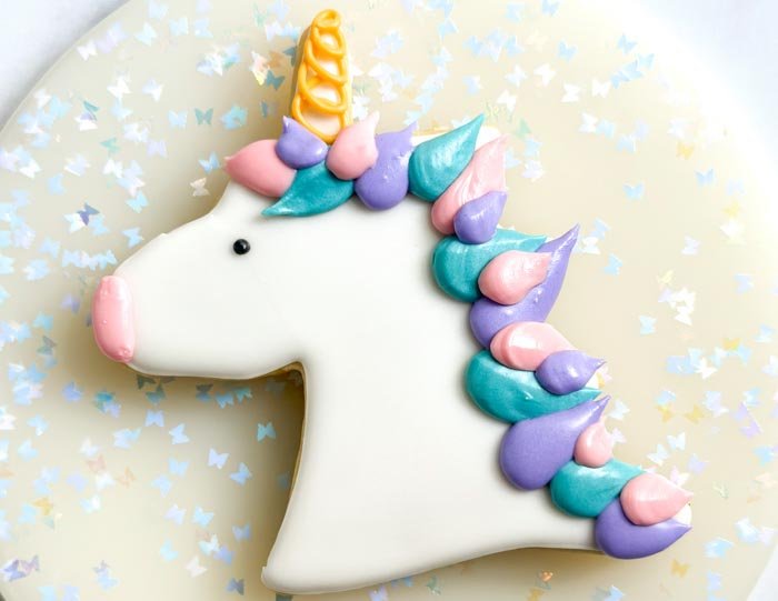 Image of Using the black outline consistency royal icing, pipe a small dot for the unicorn eye. Alternatively, you can use a small candy for the eye. Using the pink piping consistency royal icing, pipe the nose and use your scribe tool or toothpick, to smooth out the icing.  WATCH:How to Decorate a Unicorn Cookie with Royal Icing