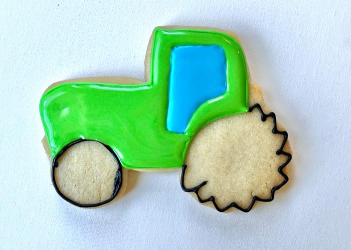 Image of Once the window area is dry and beginning to crust over, flood the green body of the tractor with green flood-consistency icing. Wait 30-60 minutes for the green icing to begin crusting over.