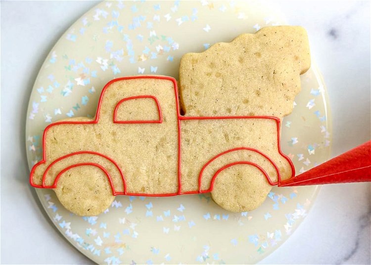 Image of Using the red piping consistency royal icing, outline the sections of the truck as shown in the photo. Be sure to not outline the tree or the wheels with red icing.