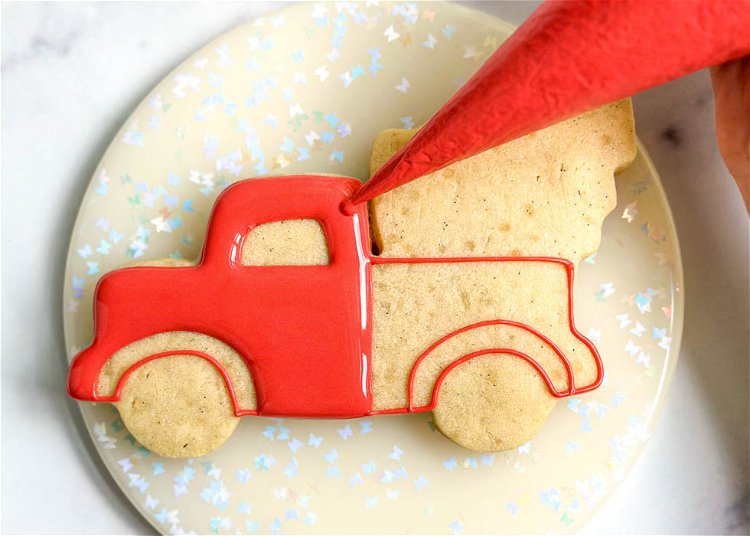 Image of Using the red flood consistency royal icing, fill in the front section of the truck. Let this section dry for 10-20 minutes until just crusted over before moving onto the next step. You can use a scribe tool or toothpick to move the icing around, ensuring full coverage and eliminating air bubbles.