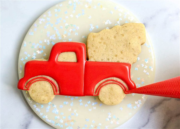 Image of Using the red piping consistency royal icing, pipe a squiggle line of icing in the middle of the small sections of the truck, above the tires. This will help prevent any cratering, or holes, that sometimes occur in small flooded sections.