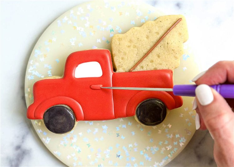 Image of Using the red piping consistency royal icing, pipe a small section for the truck door. Shape as needed with your scribe tool or toothpick. Make sure to do this carefully as the flood base is likely still wet, although it should be just crusted over.