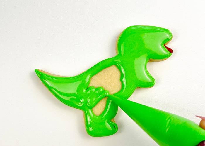 Image of Using piping consistency green icing, pipe some squiggles in the body of the T-Rex. This will help to give your flood some structure, so that the icing doesn't collapse as it cools.