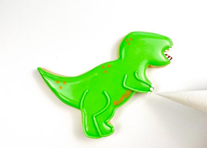Image of Using white piping consistency icing, pipe claws on the feet and paws of the T-Rex. 