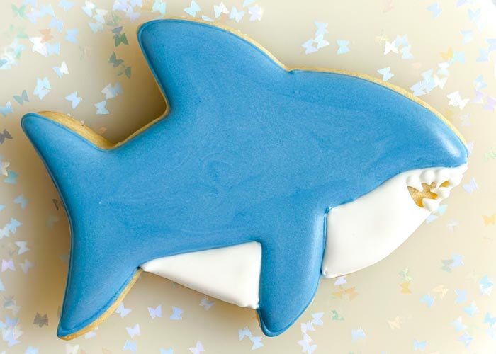 Image of Using white piping consistency royal icing, pipe dots on the shark's mouth and then use a scribe tool, or toothpick, to gently drag the icing to create the sharp teeth.