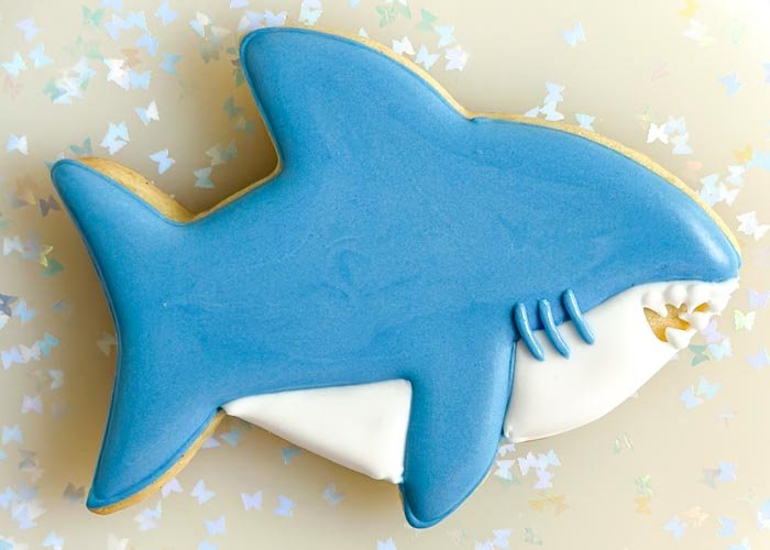 Image of Using blue piping consistency royal icing, pipe 3 identical curved lines halfway between the shark's fin and the mouth. These will be the gills.