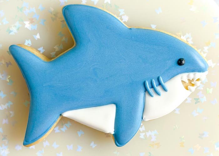 Image of Using black piping consistency royal icing, pipe a small dot above the last tooth for the shark's eye. If you want to skip mixing up a batch of black icing, you can also use a small candy or nonpareil to create the shark eye. And you're done! 